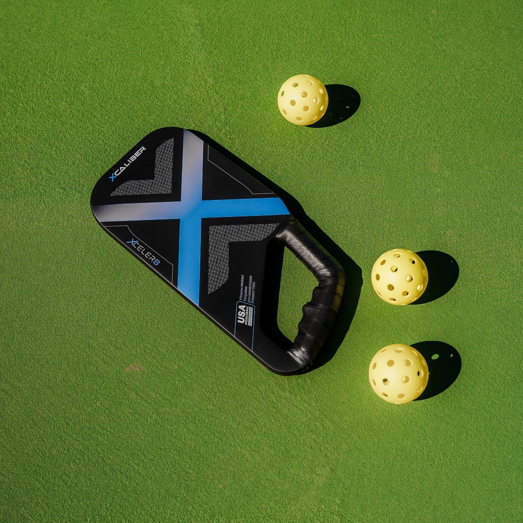 Xcaliber Ergo pickleball paddle by XCELER8 on court with pickleballs showing USA Pickleball approved badge